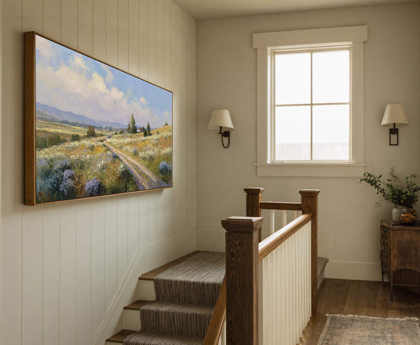 This horizontal canvas wall art showcases a vibrant landscape painting with a pastoral scene and a bright blue sky, framed in natural wood and hung on a wall with vertical.