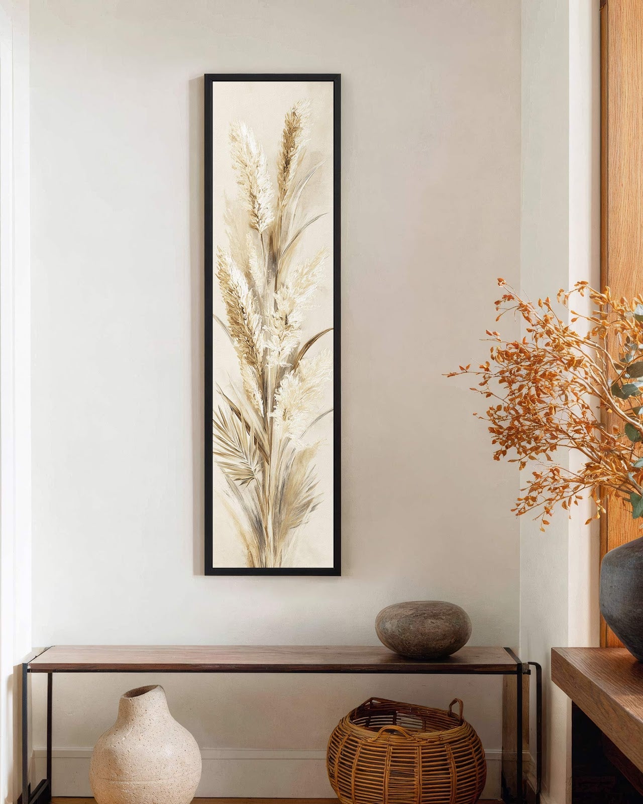 This vertical painting print of neutral pampa grass in a painterly style is displayed in a black floater frame on a white wall above a minimalist console table.