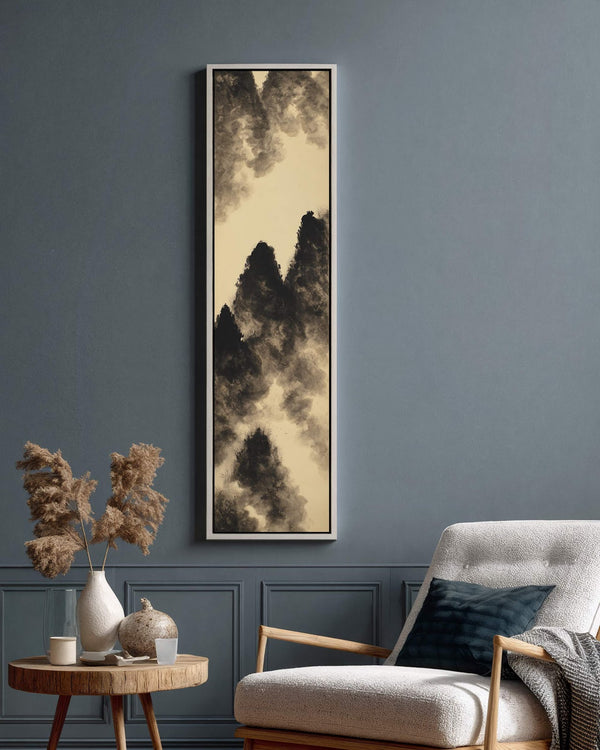A vertical ink wash mountain landscape in black and beige is showcased in a white floater frame on a blue-gray paneled living room wall next to a modern armchair.