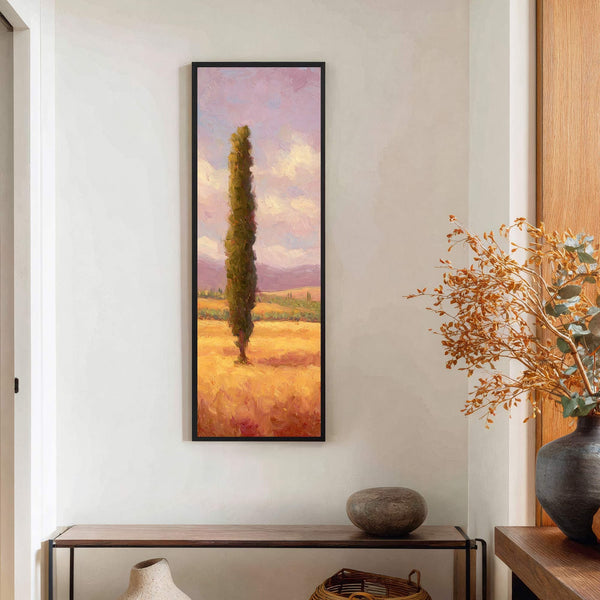 This vertical canvas wall art features an impressionistic painting of a lone cypress tree in a golden field under a pink and purple sky, framed in black, displayed above a.