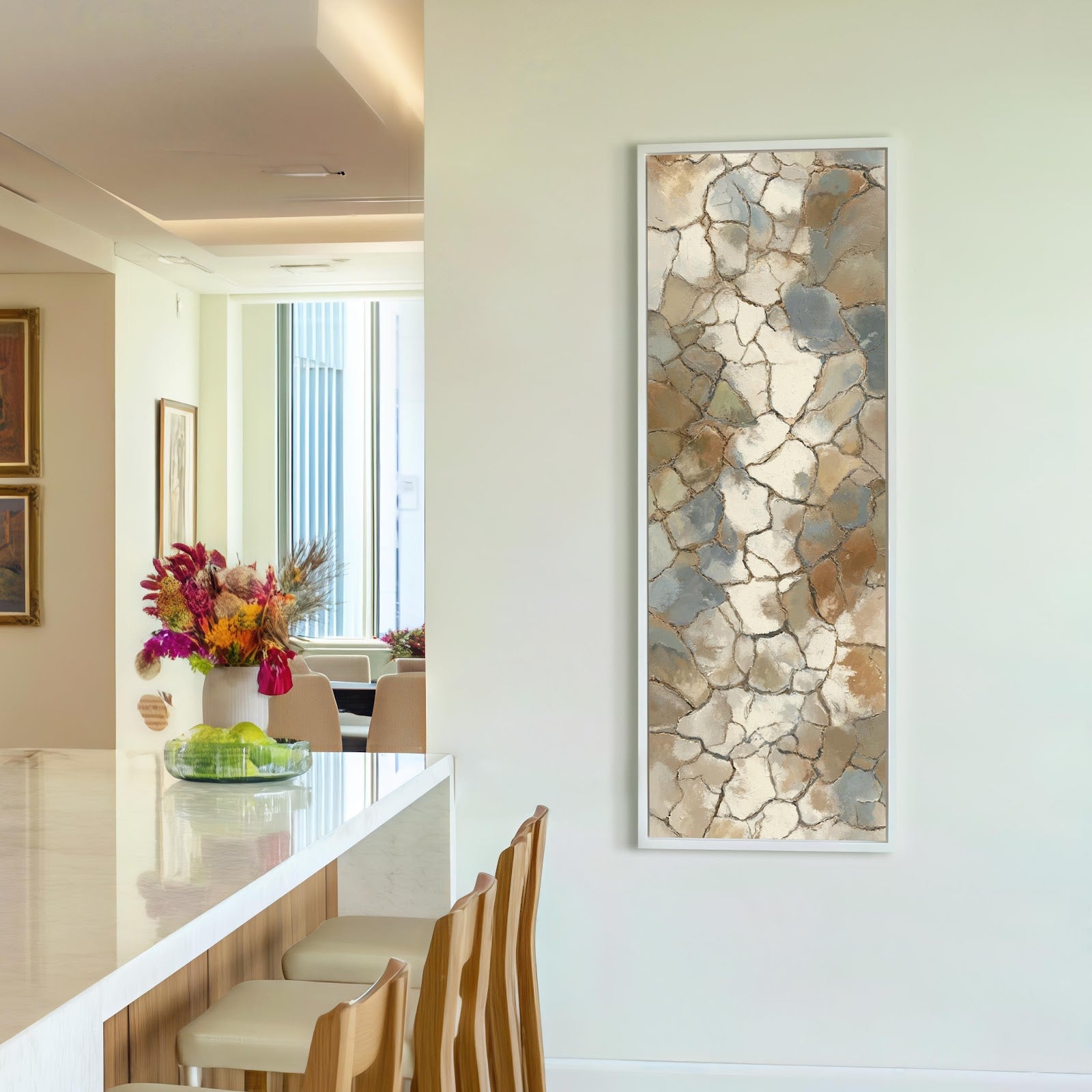 This vertical abstract canvas wall art features a neutral cracked-earth pattern in a white floater frame, hanging on a white kitchen wall beside a marble-topped island.