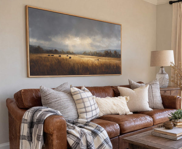 This horizontal canvas wall art depicts a dramatic landscape with dark, stormy clouds over a golden field of hay bales, rendered in a painterly style and framed with a natural.