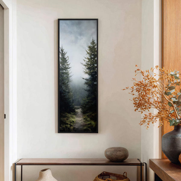 This vertical, framed canvas print depicts a misty forest path with dark green trees and a muted, atmospheric palette, displayed on a cream wall above a console table.