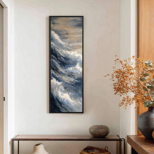 This vertical canvas wall art features an impressionistic depiction of ocean waves in a palette of blues, grays, and sandy tones, framed in black, and displayed above a narrow console.