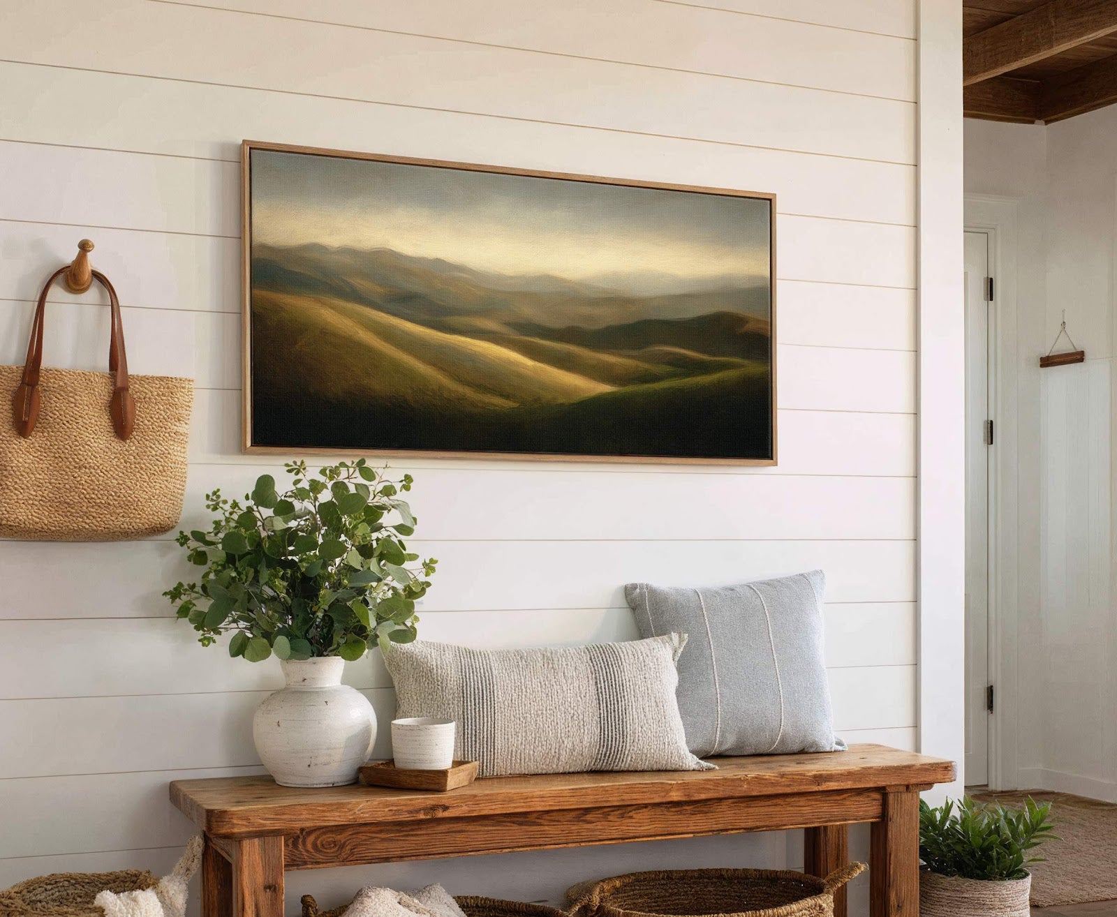 This horizontal canvas wall art features a landscape painting of rolling hills with a warm, muted palette, framed in natural wood. It is displayed in a room with white shiplap.
