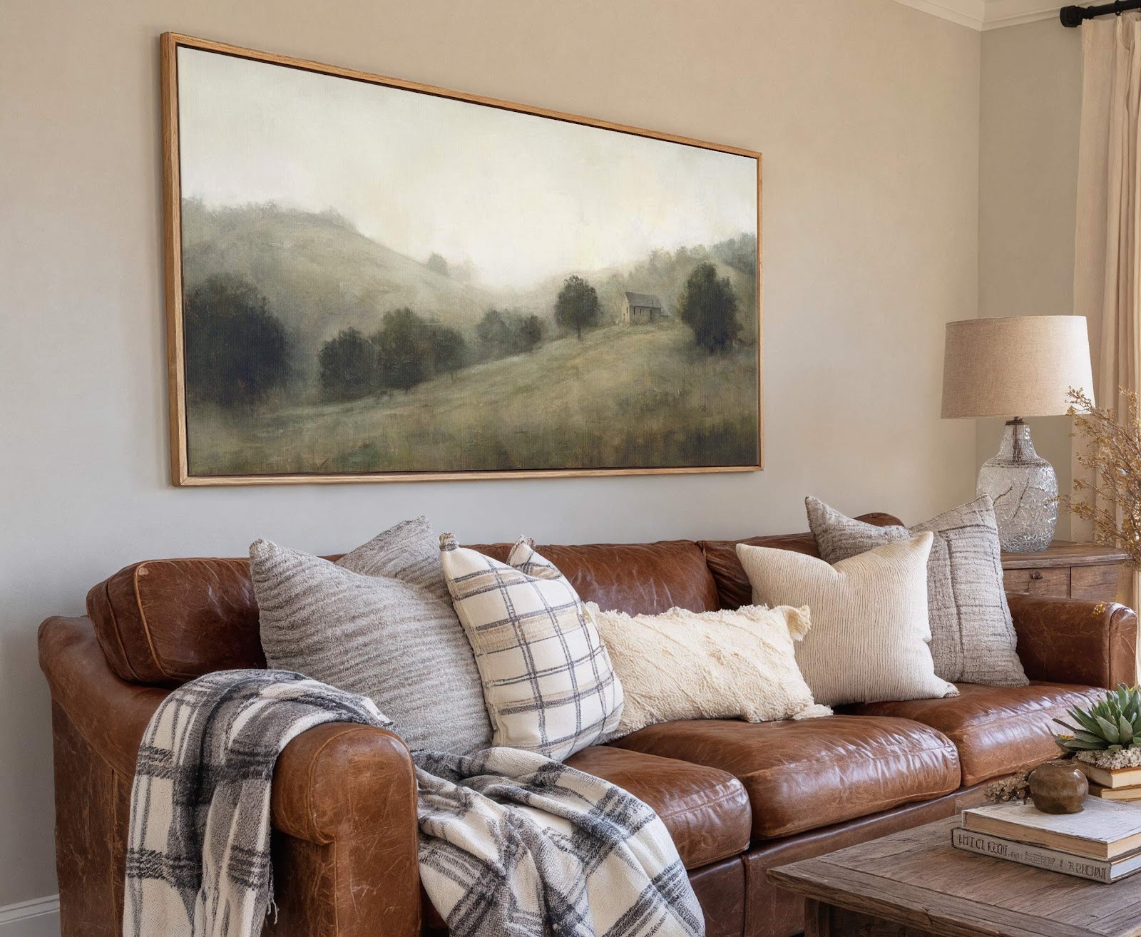 This horizontal canvas wall art depicts a misty landscape with rolling hills and trees, rendered in muted greens and grays. It is framed in natural wood and hangs above a.