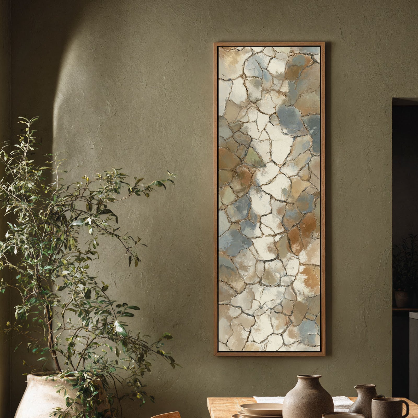 This vertical canvas wall art features a muted earth-toned abstract mosaic, displayed in a wood floater frame on a textured olive wall beside a large leafy plant.