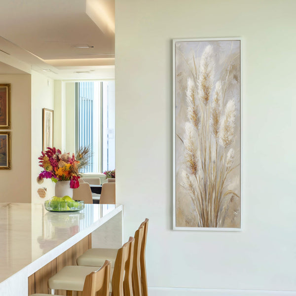 This vertical canvas wall art features reeds in a neutral palette with a soft texture, displayed on a light cream wall next to a vase of flowers on a kitchen.