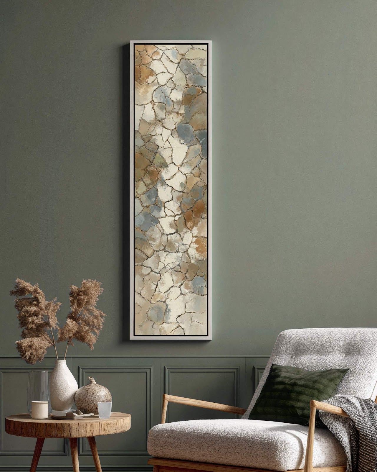 This vertical abstract art print featuring a cracked pattern in earthy tones hangs in a white floater frame on a green paneled living room wall beside an armchair.