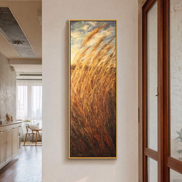 This vertical canvas wall art depicts golden reeds swaying in the wind with a bright sky above, rendered in a painterly style with warm earthy tones, and framed in gold.
