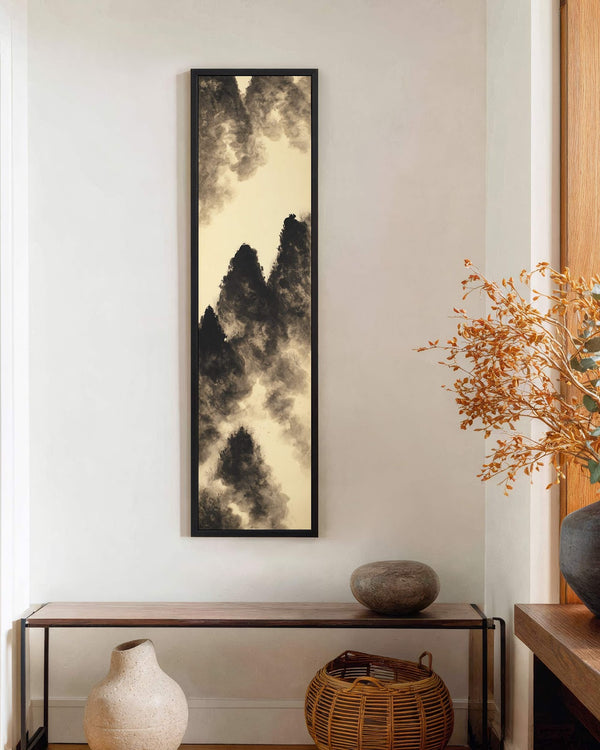 This vertical art print showcases a black and beige ink wash mountain landscape, presented in a black floater frame on a white wall above a wooden console table.