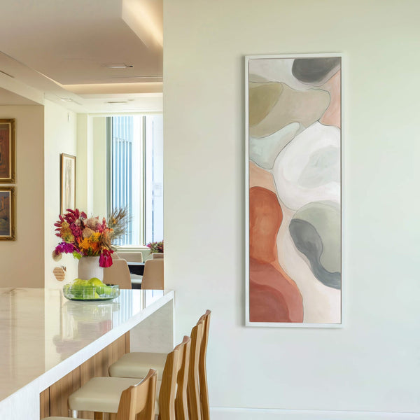 This vertical abstract art print features organic shapes in a warm, earthy palette of terracotta, beige, and gray, framed in white and displayed on a pale wall near white walls.