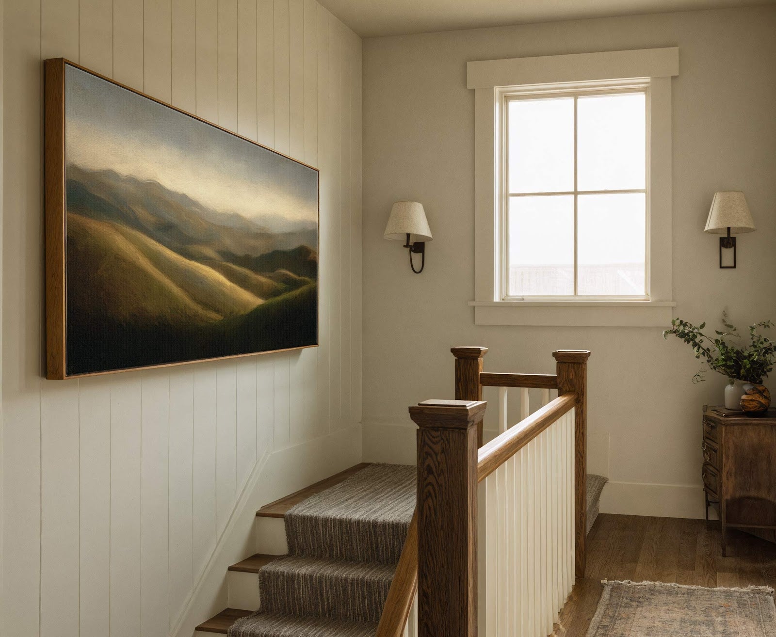 This horizontal canvas wall art depicts rolling hills with a warm, muted palette. It is set in a hallway with paneled walls and a wooden staircase, featuring a prominent window.