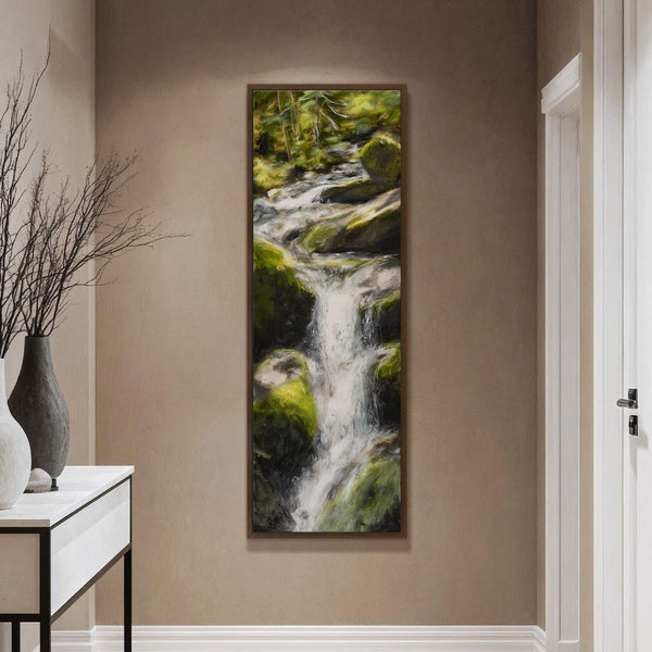 This vertical canvas print, featuring a forest waterfall rendered in lush greens and whites, is displayed on a tan wall next to a white console table with decorative vases.