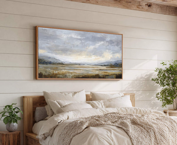 This horizontal canvas wall art features an impressionistic landscape in muted blues and earthy tones, set above a bed with a wooden headboard and a textured throw blanket, against a.