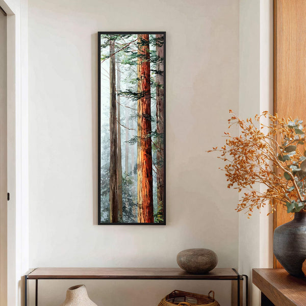 This vertical canvas wall art features a watercolor painting of redwood trees with warm orange and green tones, framed in black and displayed on a white wall above a wooden.