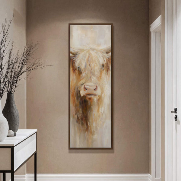 This vertical canvas wall art features a loose, impressionistic painting of a Highland cow with a warm, neutral palette, framed in dark wood and displayed on a beige textured wall.