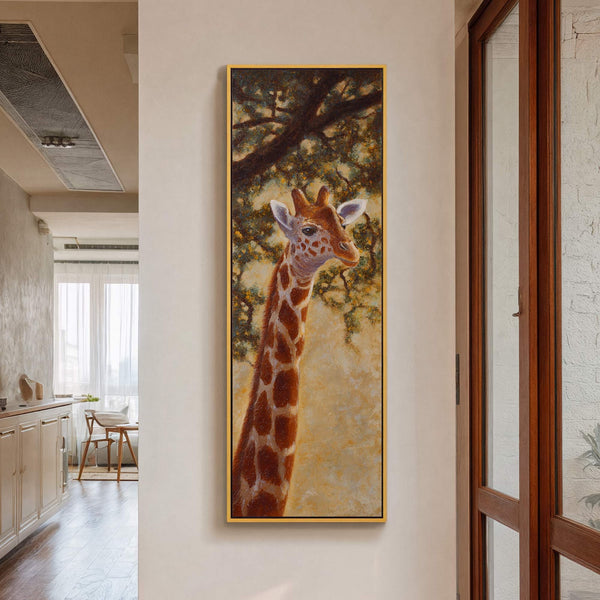A vertical, realistic art print on canvas features a giraffe against a softly textured, warm background, framed in gold. It hangs on a light-colored wall in a home, near a.