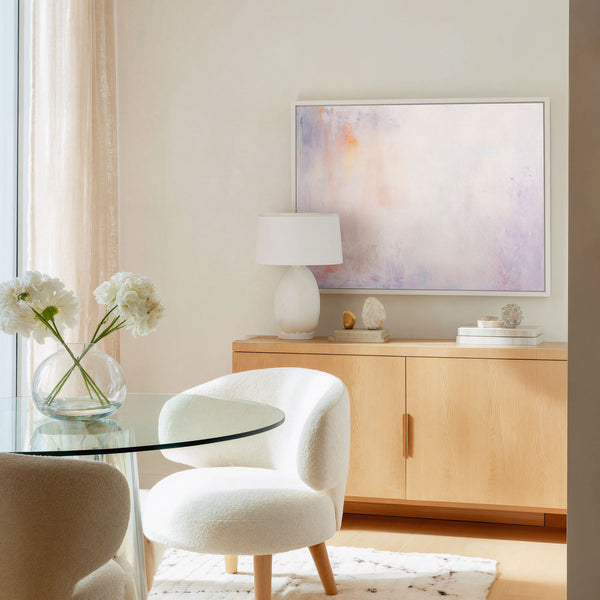 Large framed giclee art print featuring a soft abstract design in white, blush pink, and lavender, displayed above a wooden sideboard in a modern dining area