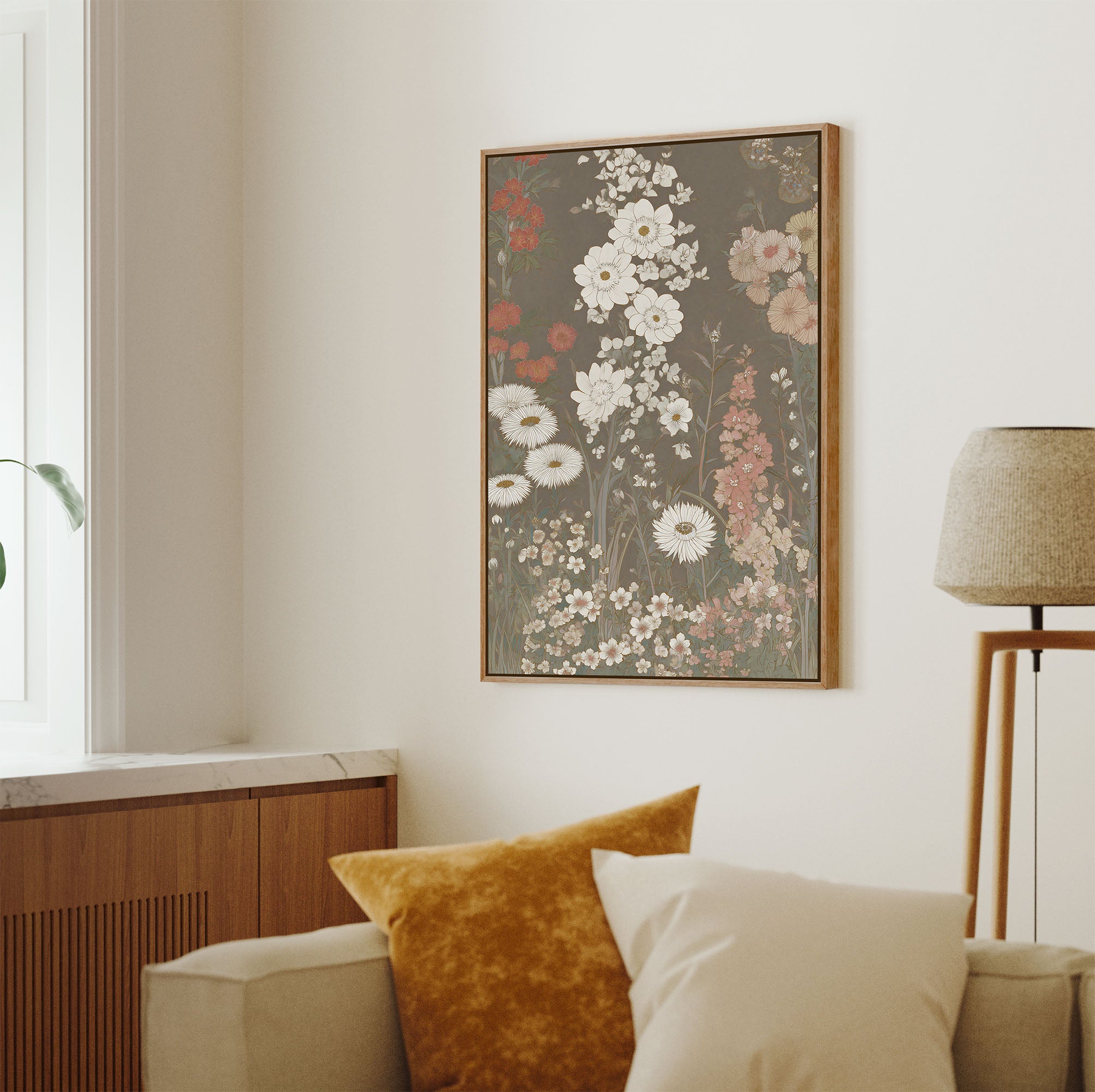 Natural pecan framed botanical art print featuring a dense tapestry of white, pink, and red wildflowers and green foliage against a textured, muted taupe-brown background, hung on a light wall above a sofa