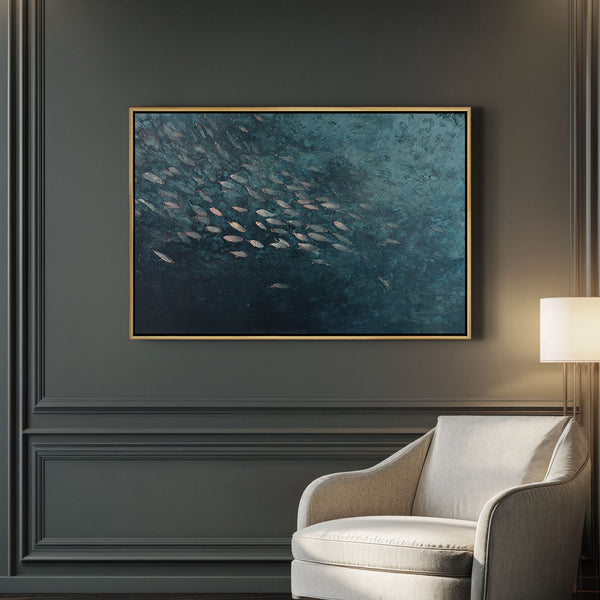 Large framed giclee art print depicting a school of fish swimming in deep blue-green textured water, displayed above a light armchair in a modern living room with dark gray walls