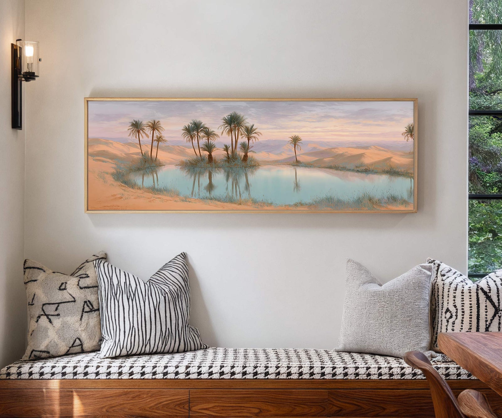 Framed desert oasis canvas wall art hung above a patterned bench in a modern interior with neutral cushions and natural light