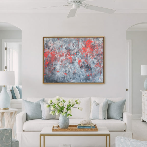 Gold-framed abstract painting featuring dynamic, textured brushstrokes in vibrant red, various grays, and white, displayed above a white sofa with light blue pillows in a bright, modern living room