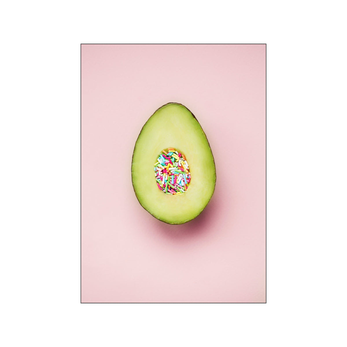 Centered avocado half with colorful sprinkles on a soft pink background