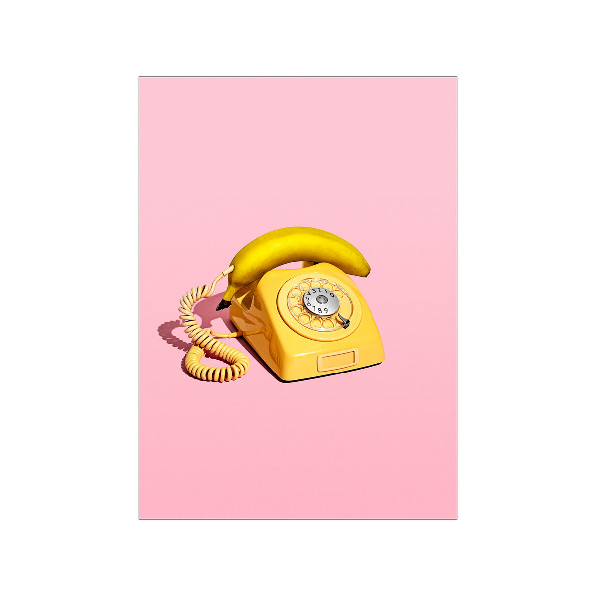 Yellow banana resting on a vintage rotary phone against a soft pink background