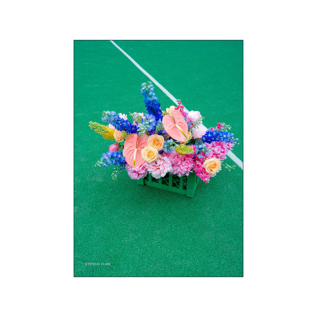 Colorful floral arrangement in a green crate on bright green turf with a diagonal white line