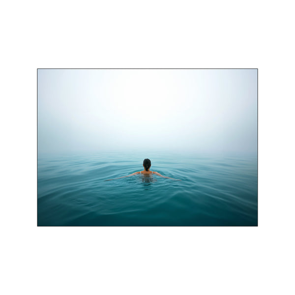 A lone swimmer with their back to the viewer glides through calm, deep blue ocean waters under a hazy, light-filled sky, embodying a feeling of peaceful solitude.