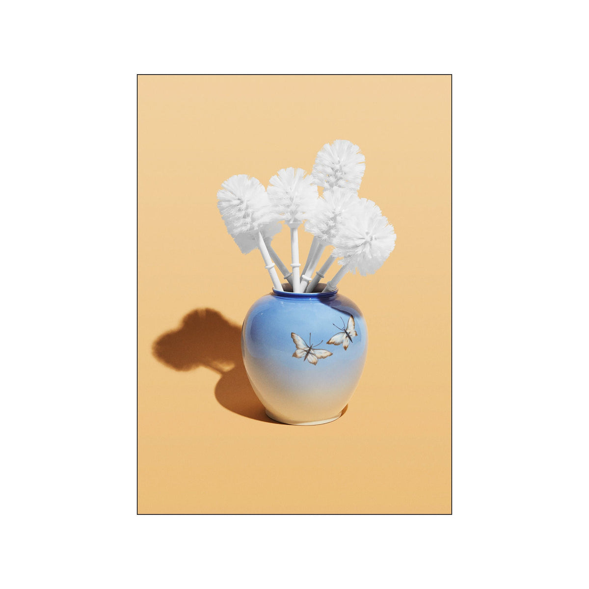 White toilet brushes arranged like flowers in a blue vase on a warm yellow background