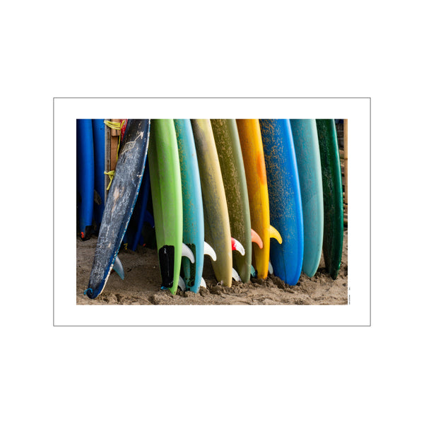 A row of colorful surfboards in various shades of blue, green, and yellow are propped up on a sandy beach, evoking a relaxed, bohemian, and coastal vibe.