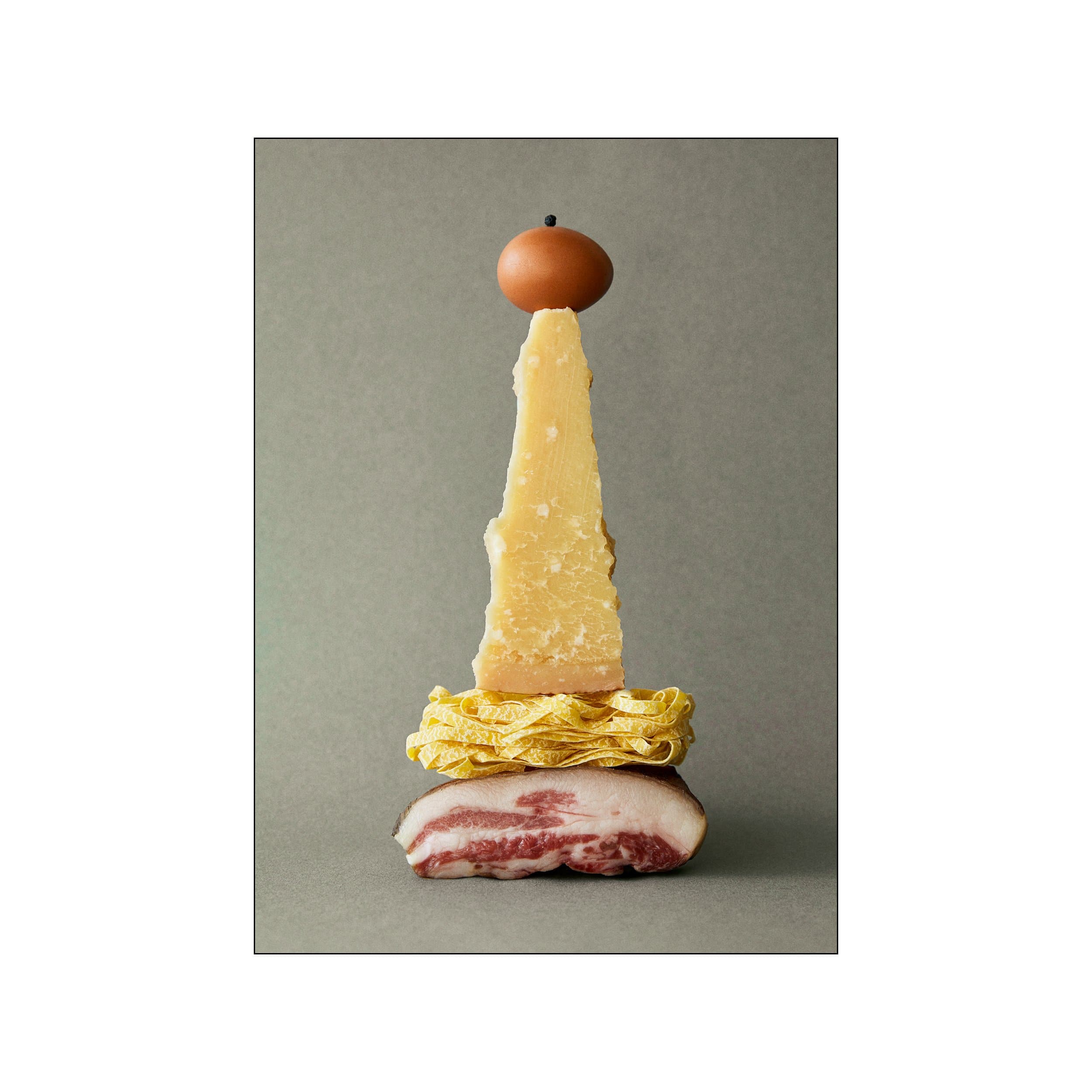 Minimal carbonara ingredient still life with egg, cheese, pasta, and cured pork on gray background